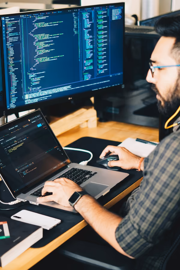 Développeur codant sur un double écran avec laptop, interface de code visible sur fond sombre